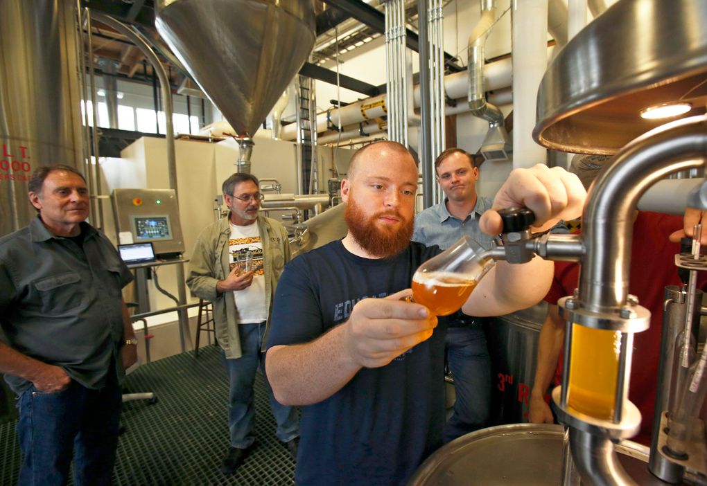 Wayne Carpenter, left, Bob Rock of the Skagit Valley Malting Company and Emerson Lamb, co-founder of Westland Distillery, watch as Matt Hofmann, master distiller at Westland Distillery, draws the first sample of a wort made from barley grown in the Skagit Valley. (Mark Harrison/The Seattle Times)