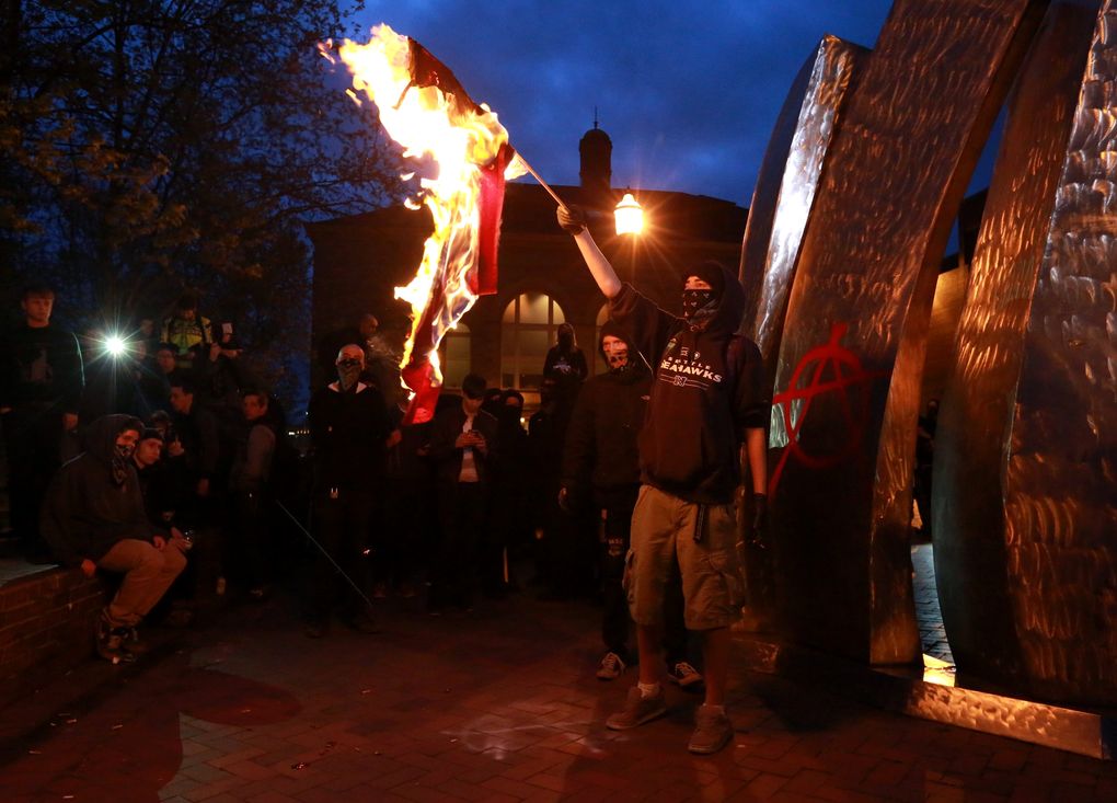Anarchists light a fire and draw an “A” symbol in red spray paint on the silver sculpture outside Seattle Central College after being penned in by police near Broadway and Pine Street. (Bettina Hansen / The Seattle Times)