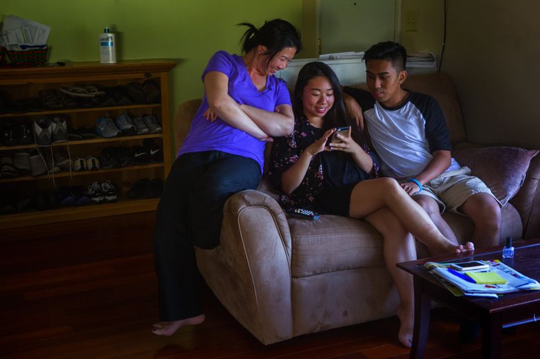 Linh Sam, left, hangs out with her daughter, Lena Tran, and Lena’s boyfriend in their home as they check out clothes for sale on Lena’s phone. Lena, an only child, is being raised by her mother. (Ellen M. Banner/The Seattle Times)