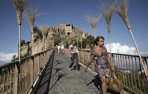 Visitors walk down the footbridge that leads to Civita di Bagnoregio, Italy, Sept. 3, 2015. Tourists have flocked to Civita, a stunning hilltop village that is slowly crumbling, with an estimated 500,000 visitors this year adding to a year-round population of about eight. (Nadia Shira Cohen/The New York Times)