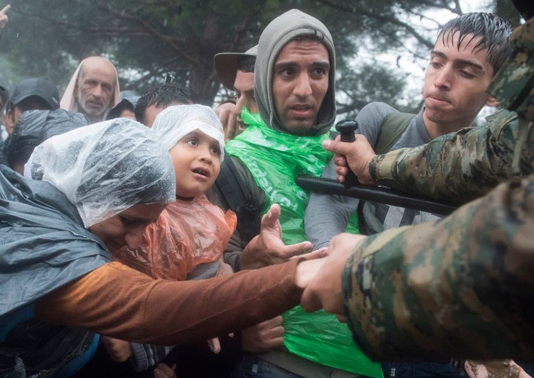 Macedonian border police helps refugees and migrants to pass in  heavy rainfall from the northern Greek village of Idomeni to southern Macedonia, Thursday, Sept. 10, 2015. Thousands of people, including many families with young children, braved torrential downpours to cross Greeceís northern border with Macedonia early Thursday, after Greek authorities managed to register about 17,000 people on the island of Lesbos in the space of a few days, allowing them to continue their journey north into Europe. (AP Photo/Giannis Papanikos)