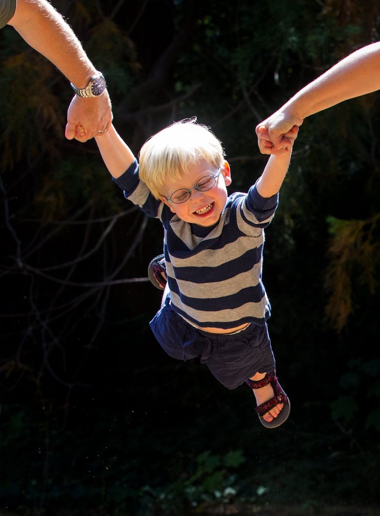 Ian Keljo, 3, is all smiles as he swings from his parents’ arms at Lincoln Park in West Seattle. (Ellen M. Banner/The Seattle Times)