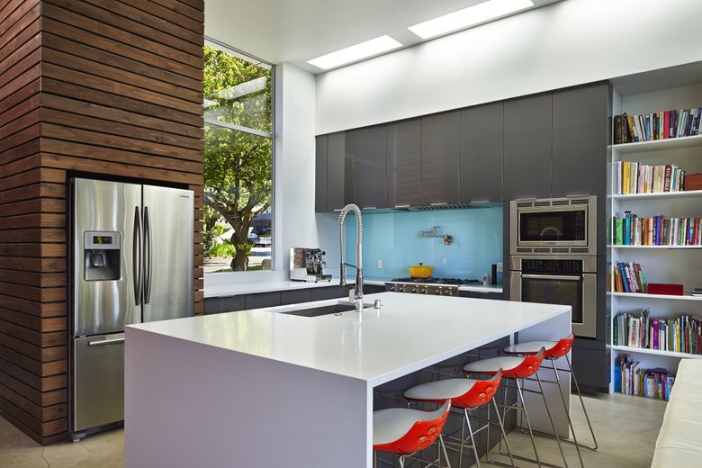 The open kitchen is light and bright with a tall streetside window and five long skylights along the east wall, a ribbon of light that connects front to back. Counters and the big, fat island are Caesarstone. The robin’s-egg blue backsplash is glass backpainted with latex paint. (Benjamin Benschneider / The Seattle Times)