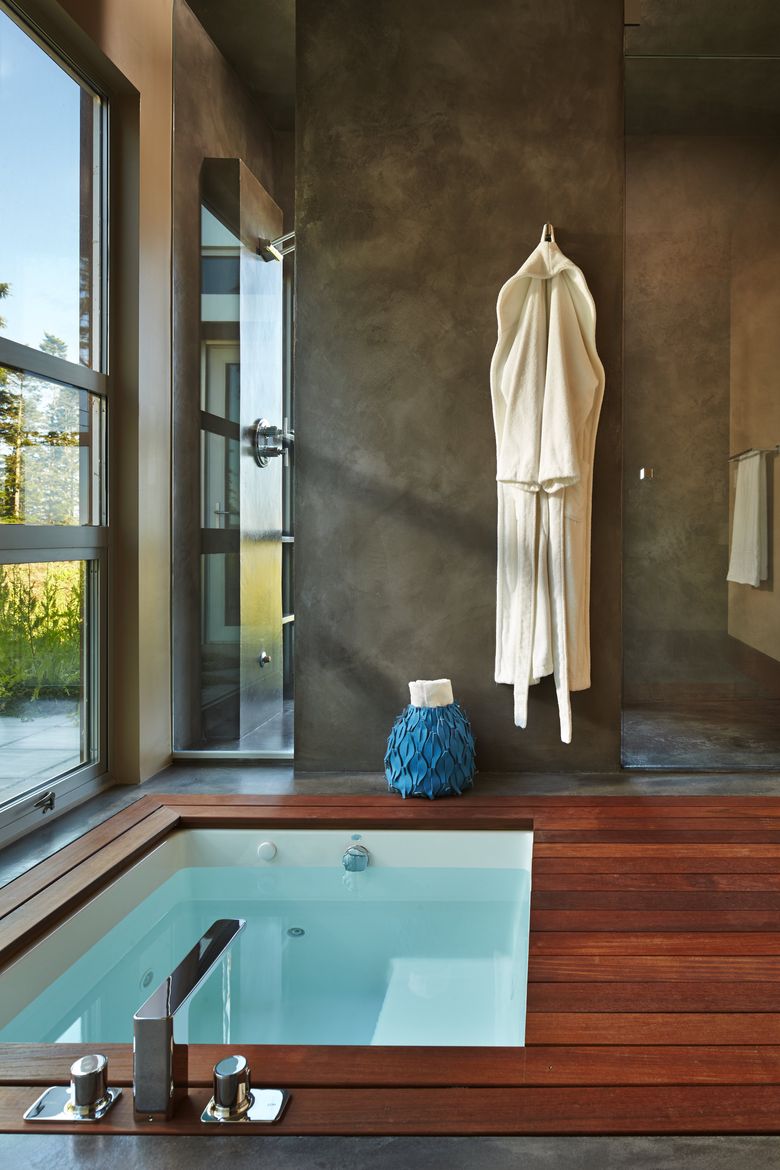 Ipe decking surrounds the sunken tub. The room features charcoal gray Milestone walls and floors. Beyond is a shower with full-height windows. (Benjamin Benschneider / The Seattle Times)