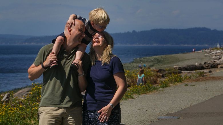 While riding on dad Jonathan Keljo’s shoulders, Ian leans to give mom Amy a kiss as they stroll near the beach at Lincoln Park in West Seattle.  (Ellen M. Banner/The Seattle Times)
