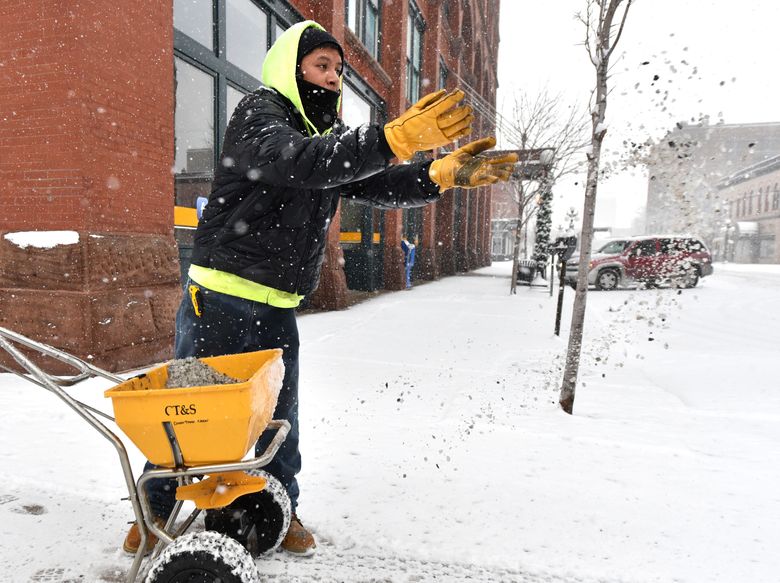 Hugo Pineda, an employee of Dakota Dunes’ CTS, tosses out rock salt while working to clear snow from a sidewalk along Historic Fourth Street in downtown Sioux City, Iowa, Monday, Nov. 30, 2015. The Sioux City area is forecast to receive up to 12-inches of snow Monday through Tuesday. (Tim Hynds/Sioux City Journal via AP)