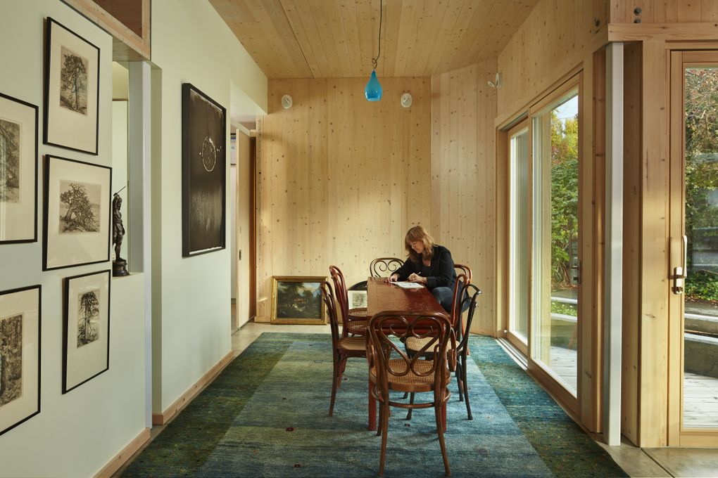 Susan Jones works at the dining-room table under a dangling seaglass light. She brought much of the home’s furniture back from an architectural stint in Vienna; other pieces came via her grandmother. Most are a darker reddish wood to contrast with the CLT, and most have a curved linear quality to contrast with the home’s straight and strong boards. (Benjamin Benschneider/The Seattle Times)