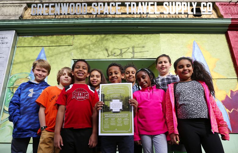 Contributing authors, Monday, April 4, 2016, in Seattle, who attend the after-school writing and tutoring program at The Greater Seattle Bureau of Fearless Ideas, stand in front of their boarded-up building damaged from the Greenwood explosion; ground-zero is across the street. They hold a poster for a book-launching party, a book they contributed to and are donating all proceeds from to the fund established to help those affected by the recent gas explosion. From left: Skylar Perry, 10; Solan Honore-Jones, 9; Anub Zekaryas, 7; Melawit Samuel, 8; Nehemiah Daniel (holding poster), 9; Keziah Yelemwossen, 9; Tselot Bezabeh, 8; Maya Mullaney, 10; and Phoebe Yelemwossen.