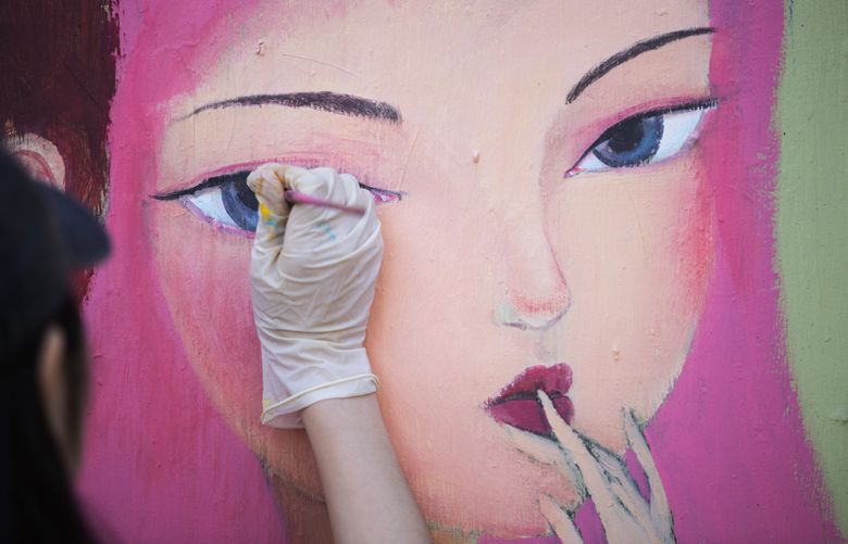 Eva Yue Wang, an artist originally from the Henan province in China, fills in the eye of a girl depicted on her first large-scale mural, in between bus stop shelters on N. 85th St. next to Urban Hands in Greenwood on April 19, 2016. Wang received her MFA in illustration from Syracuse University.
After the Greenwood explosion on March 9, Joey DeYoung, the executive director of the Greenwood nonprofit Urban Hands, helped organize a cleanup event that week to beautify the area. A friend of his jokingly suggested they paint all the plywood covering damaged businesses, so DeYoung stopped by art studios on a whim to share the idea. The next day, a group of artists helped paint some 20 storefronts during the cleanup event. “I think it made a big difference in lifting people’s spirits,” said DeYoung.
Other artists and businesses began to ask how they could participate, so DeYoung coordinated with local artist Ahmed Bashir Davis to find other artists to create art on the street, as well as makeshift art gallery on the plywood inside Urban Hands’ second-story Greenwood space. “It’s really nice to give someone the opportunity to do what they love,” says Davis. “It’s the community painting for the community.”
Urban Hands hopes to put all the murals created for the neighborhood up for auction at the PhinneyWood Big Art Walk on May 13. Proceeds will to go the Greenwood Relief Fund.