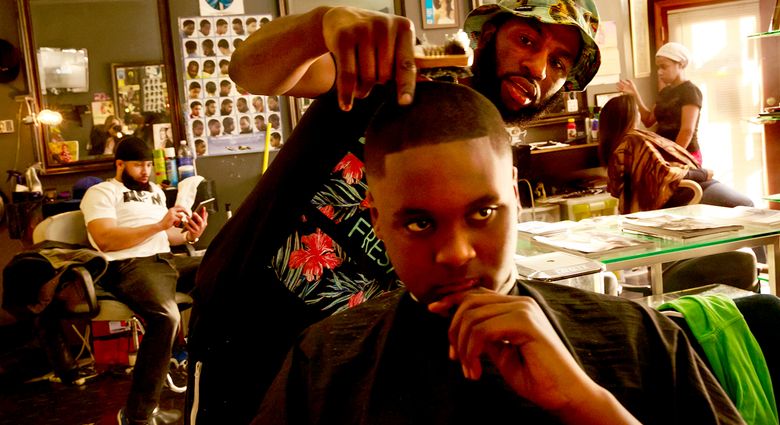 Spac3man cuts the hair of Pharell Gayle, 13, at Frank’s Barber Shop at 23rd Avenue and South Jackson Street, Seattle. Owner Frank Taylor started this shop, his second, in January, anticipating the purchase of the shopping complex where his first shop was located. (Erika Schultz/The Seattle Times)