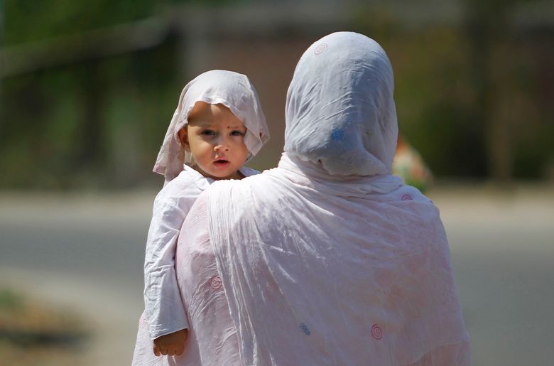 A mother and a child with his head covered with a wet towel to protect it from a heat wave, wait for transportation in Jammu, India, Thursday, May 19, 2016. Scorching summer temperatures, hovering well over 40 degrees Celsius, (104 Fahrenheit) are making life extremely tough for millions of people across north India. (AP Photo/Channi Anand)