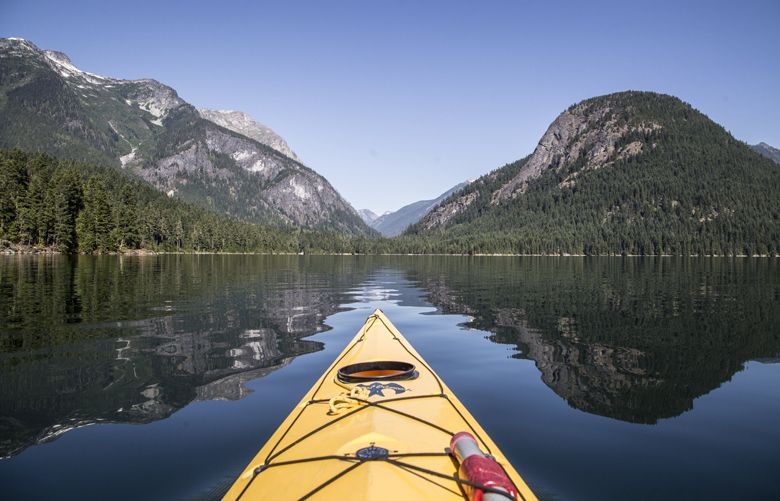 Kayaking on Ross Lake between the shadows of an unidentified peak at left and Pumpkin Mountain at right. In the saddle between is the Big Beaver Creek trail in the North Cascades National Park.