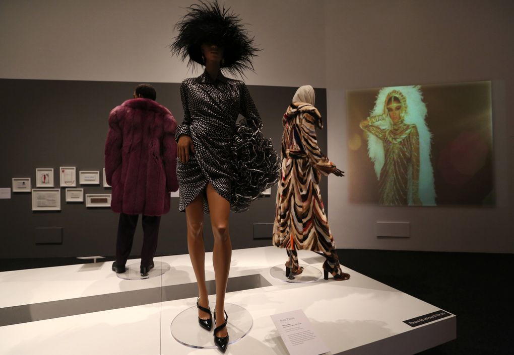 A 1980s day dress and muff from Jean Patou, flanked by a bold purple coat and suit by Giorgio Casani, left, and a coat with matching boots from Laura Biagiotti, part of “Inspiring Beauty: 50 Years of Ebony Fashion Fair,” a touring exhibit from the Chicago History Museum, at BAM. (Alan Berner/The Seattle Times)