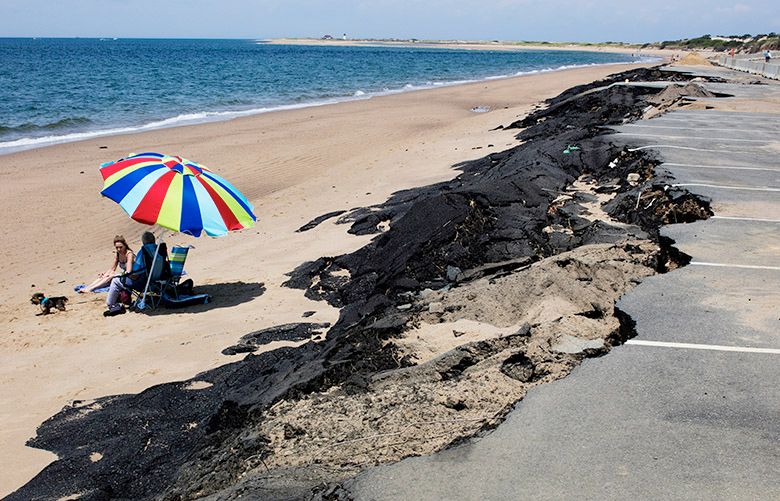 Linda and Tony Cannata lounge by a section of parking lot collapsed by erosion at Herring Cove Beach at the tip of Cape Cod near Provincetown, Mass., July 1, 2016. Across the country, parks officials coping with erosion are increasingly turning to â€œmanaged retreatâ€ â€” here, the lot is being moved back 125 feet and elevated, allowing the beach to claim the existing lot. (M. Scott Brauer/The New York Times)