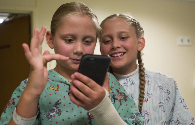 Olivia Wagoner looks over her sister Priscilla’s shoulder as they use the new Pokemon Go app to hunt pokemon in the Burn Center at Harborview Medical Center, Monday, July 18, 2016. The pair of Montanan twins suffered burn wounds after a boat fire during a camping trip, and were flown to Seattle for treatment.