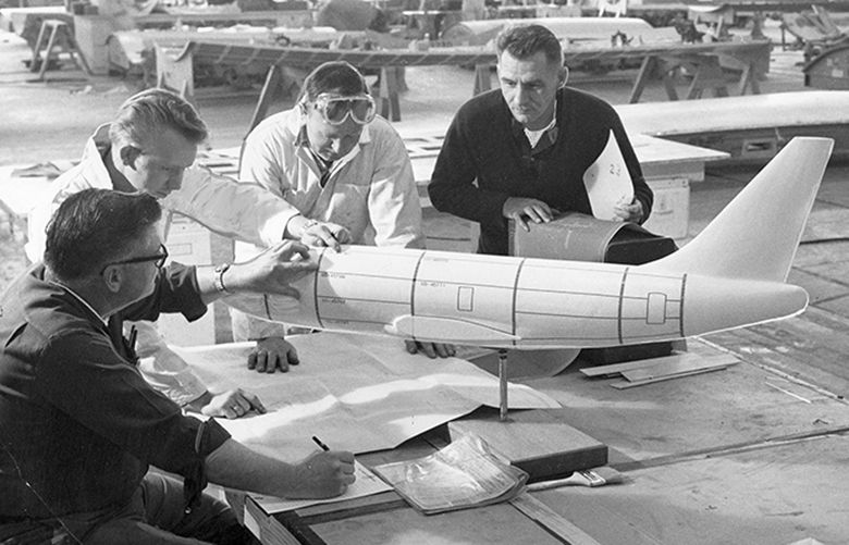 Historical Gallery
Seattle Times File, 1966 
BOEING COLLECTION
ORIGINAL CAPTION: Boeing Co. employees are shown with a model of the firm’s new Model 737 short-range twinjet, which is used as a factory training aid to show skin-panel placement and part numbers. The first 737 is taking shape in the Renton factory, with rollout scheduled late this year. Boeing Co. Photo.