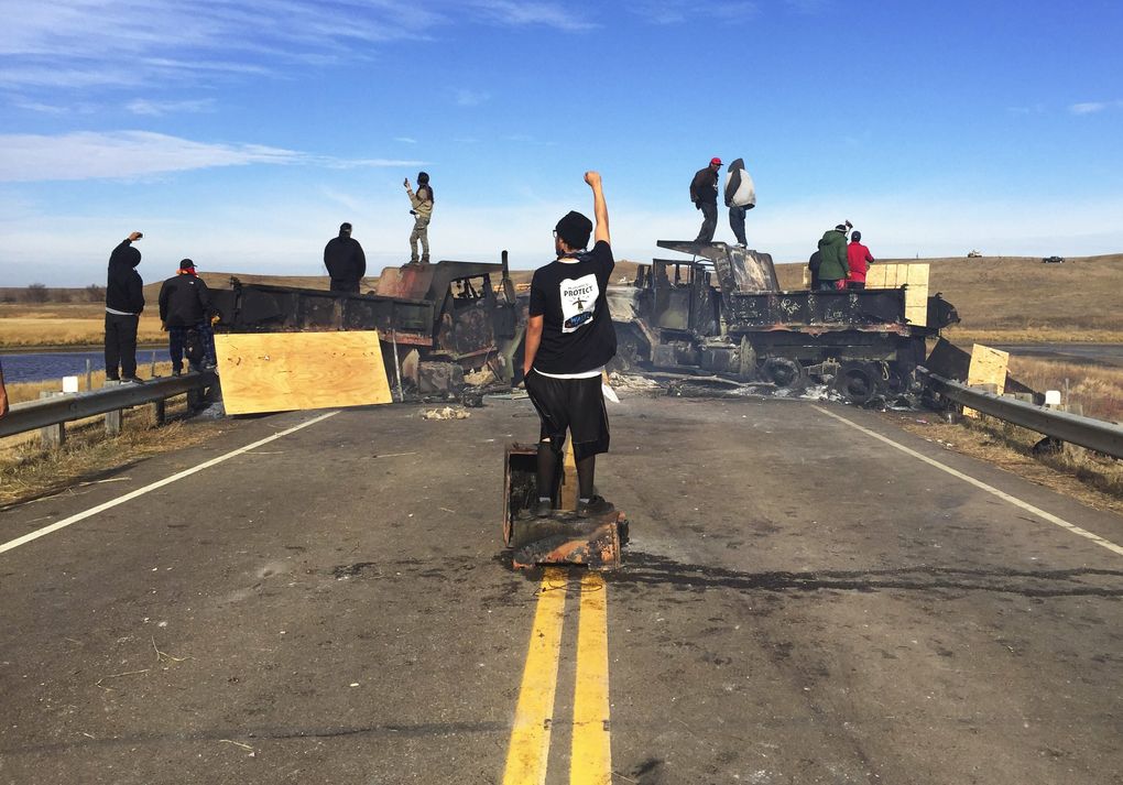 Burned-out trucks, still smoldering, and protesters block a bridge on Highway 1806 on Friday. (Alan Berner/The Seattle Times)