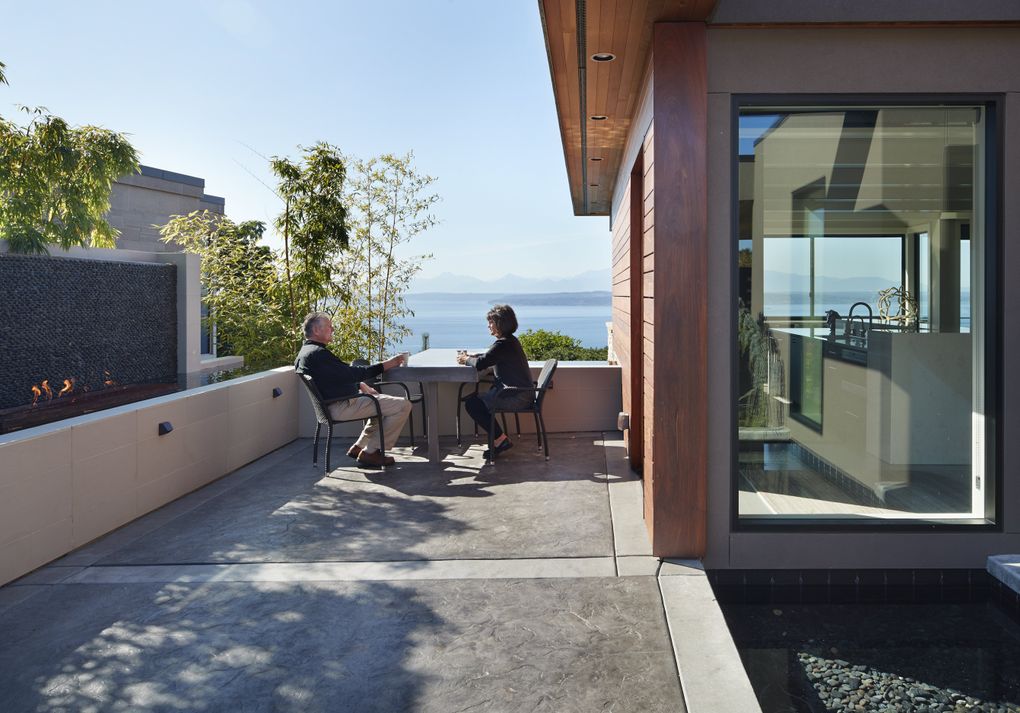 Rhonda and Larry Nelsen relax at the built-in concrete table (by Absolutely Fine Concrete) on their deck; it sports their initials: L & R. The gas firepit in the infinity pool lights at night. (Benjamin Benschneider/The Seattle Times)