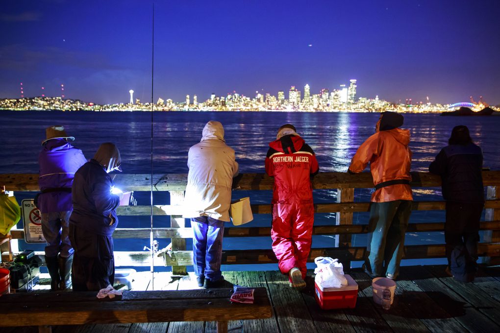 Fishermen, including Tony Truong, in red, and his brother Ricky Truong, in orange, fish for squid at Seacrest Park Pier in West Seattle. Tony Truong says his family often fishes for squid at night in the fall and winter months. “We don’t mind the weather,” he says. (Erika Schultz/The Seattle Times)