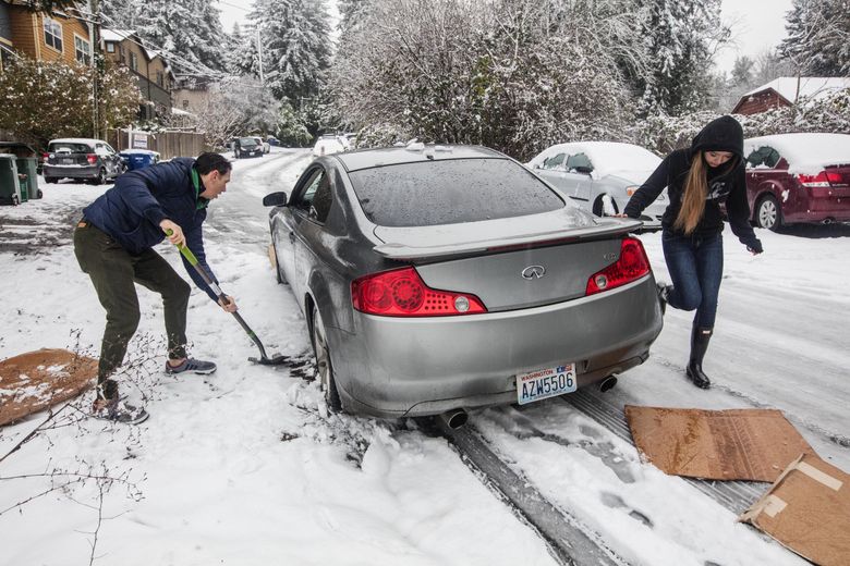 Erik Guzman uses his shovel to help keep a neighbor’s car from slipping into the ditch on Northeast 135th, where packed snow with rain was very slick. (Steve Ringman / The Seattle Times)