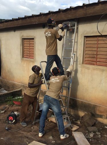 Workers drill holes along the roofline of a house in Kenya to install eave tubes to kill malaria-transmitting mosquitoes. In initial trials, mosquito populations in the village crashed. (Penn State University)