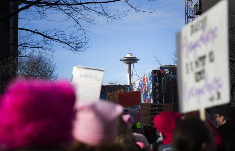 People wearing pink “pussyhats” walk down Fourth Avenue in downtown Seattle, with the Space Needle in the distance, during the Womxn’s March on Jan. 21, 2017. (Lindsey Wasson / The Seattle Times)