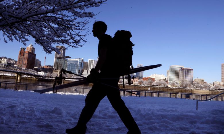 A pedestrian walks the snow-covered promenade with skis, poles and backpack on the east side of the Willamette River in Portland on Thursday. (Don Ryan/The Associated Press)