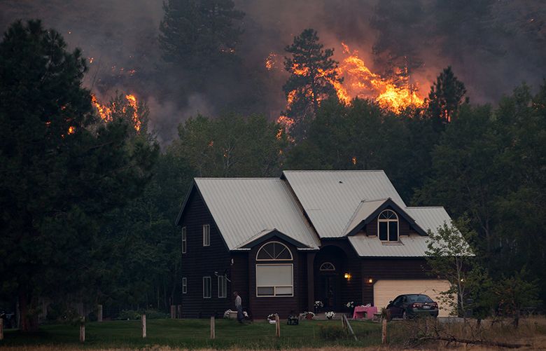 A person walks in front of a home in Twisp where the hillside burned early in the morning Thursday, Aug. 20, 2015.