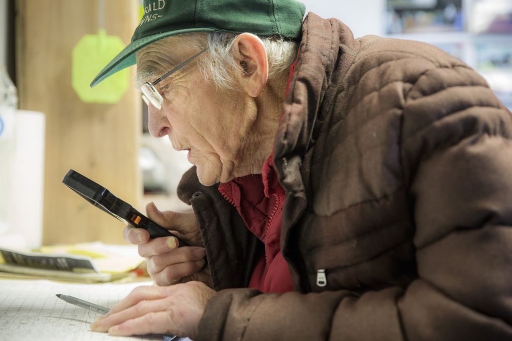 Don Munger, 93, goes over his charts with a magnifying glass in his office in the stables at Emerald Downs – he is one of three horse trainers there in their 90s. Munger is a World War II vet who fought on Iwo Jima. “It keeps me going, these horses,” said Munger. (Bettina Hansen/The Seattle Times)