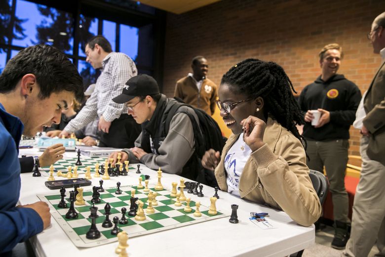 Phiona Mutesi, center, plays chess with Walter Borbridge, left, during their first chess-team meeting in September. Mutesi and Benjamin Mukumbya, standing in background, grew up together in a Uganda slum and learned to play competitive chess in a local program that led them to international success.  (Bettina Hansen/The Seattle Times)