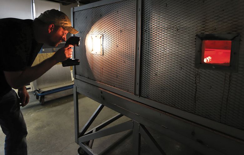 Glassworks production manager James (Jay) Martell peers into a viewing portal to check the molten glass counters inside a giant kiln. (Mike Siegel/The Seattle Times)