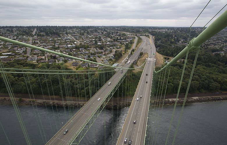 TACOMA NARROWS BRIDGE — LABORING UP HIGH — LO — 08202014 — 141130According to Wikipedia, “The Tacoma Narrows Bridge is a pair of twin suspension bridges that span the Tacoma Narrows strait of Puget Sound in Pierce County, Washington. The bridges connect the city of Tacoma with the Kitsap Peninsula and carry State Route 16 (known as Primary State Highway 14 until 1964) over the strait. Historically, the name “Tacoma Narrows Bridge” has applied to the original bridge nicknamed “Galloping Gertie”, which opened in July 1940 but collapsed because of aeroelastic flutter four months later, as well as the replacement of the original bridge which opened in 1950 and still stands today as the westbound lanes of the present-day twin bridge complex.The original Tacoma Narrows Bridge opened on July 1, 1940. It received its nickname “Galloping Gertie” because of the vertical movement of the deck observed by construction workers during windy conditions. The bridge became known for its pitching deck, and collapsed into Puget Sound the morning of November 7, 1940, under high wind conditions. Engineering issues as well as the United States’ involvement in World War II postponed plans to replace the bridge for several years; the replacement bridge was opened on October 14, 1950.By 1990, population growth and development on the Kitsap Peninsula caused traffic on the bridge to exceed its design capacity; as a result, in 1998 Washington voters approved a measure to support building a parallel bridge. After a series of protests and court battles, construction began in 2002 and the new bridge opened to carry eastbound traffic on July 15, 2007, while the 1950 bridge was reconfigured to carry westbound traffic.”Looking east towards Tacoma in photo.MethodeID: 4.0.2360458#News#News#20140901#4.0.2360567