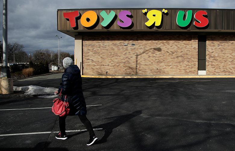 FILE- In this Jan. 24, 2018, file photo, a woman walks in a parking lot of a Toys R Us store in Wayne, N.J. Toys R Us CEO David Brandon told employees Wednesday, March 14, 2018, that the company’s plan is to liquidate all of its U.S. stores, according to an audio recording of the meeting obtained by The Associated Press. (AP Photo/Julio Cortez, File)