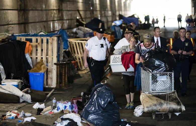 A couple, center, who were living under a bridge carry their possessions out as police move in to clear the encampment in Philadelphia, Wednesday, May 30, 2018.  The cityâ€™s homeless packed up their few belongings as sanitation workers cleaned and power washed what had been a heroin encampment only moments before. The morning activity attended by police was part of a month-long pilot program meant to relocate addicts living under two bridges in Philadelphia. (AP Photo/Matt Rourke) PX101 PX101