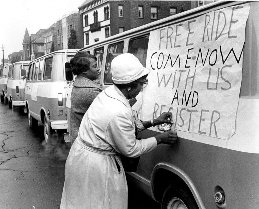 Emma Eddins, left, and Odessa Brown taped a sign to the side of one of 10 buses used by the Central Area Motivation Program at the beginning of a three-day voter registration campaign. Community organizers and aides were encouraging unregistered Central Area residents to register to vote in the 1968 election regarding 13 Forward Thrust proposals. (Seattle Times archives, 1967)