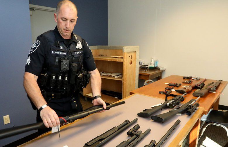 On May 23, 2018,  Seattle Police Crisis Response Team Sgt. Eric Pisconski displays guns seized from people deemed to be a danger to themselves or others. (Greg Gilbert / The Seattle Times)