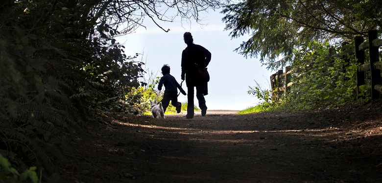 A woman and a child walk with their dog after spending time at the dog park in Westcrest Park in West Seattle. (Ellen M. Banner/The Seattle Times)