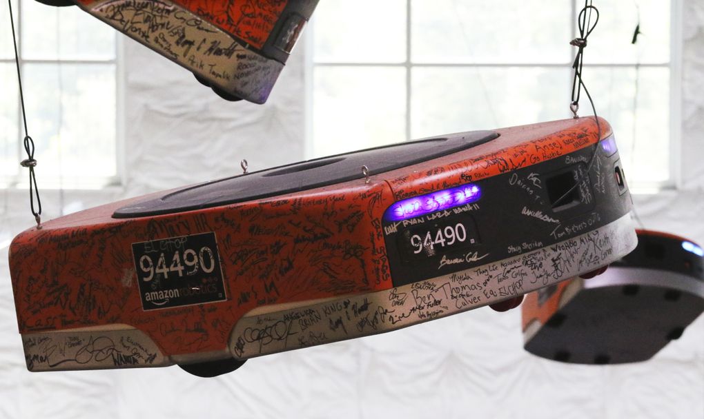 Robots signed by workers have been turned into sculptures that hang from the ceiling at the entrance to the highly automated Kent warehouse. (Alan Berner / The Seattle Times)