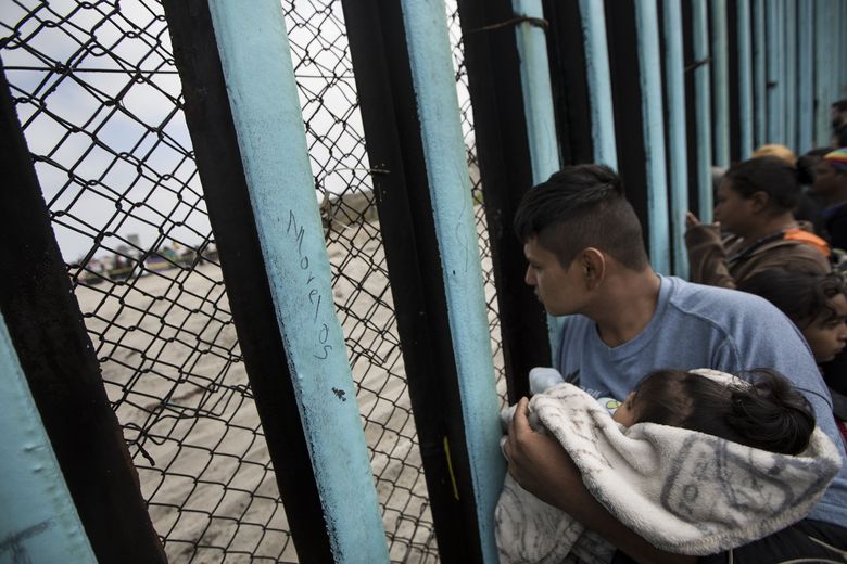 A Central American immigrant holding a child looks through the border wall into the U.S. from Tijuana, Mexico, in April.  (Hans-Maximo Musielik / AP, file)