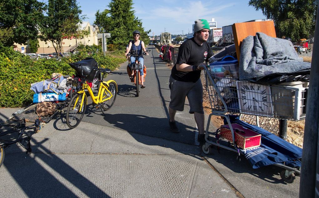 A man uses a grocery cart to move his possessions across the Burke-Gilman Trail from his former encampment behind the Fred Meyer store in Ballard. The city posted a sign to vacate the property by 9 a.m. Tuesday, so the campers moved their belongings to the other side of the trail and railroad tracks. (Mike Siegel / The Seattle Times)