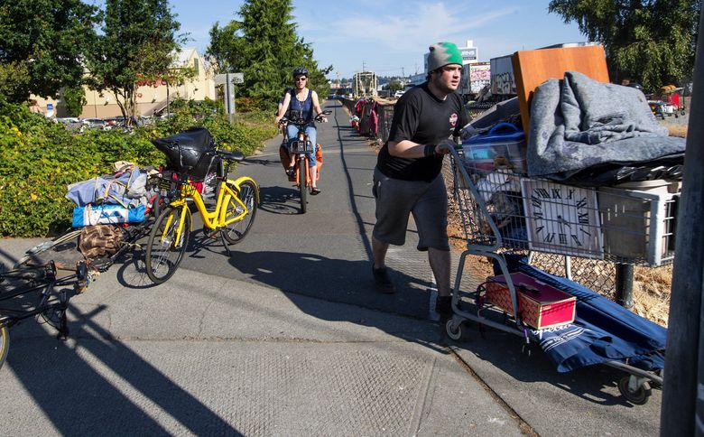A man uses a grocery cart to move his possessions across the Burke-Gilman Trail from his former encampment behind the Fred Meyer store in Ballard. The city posted a sign to vacate the property by 9 a.m. Tuesday, so the campers moved their belongings to the other side of the trail and railroad tracks. (Mike Siegel / The Seattle Times)