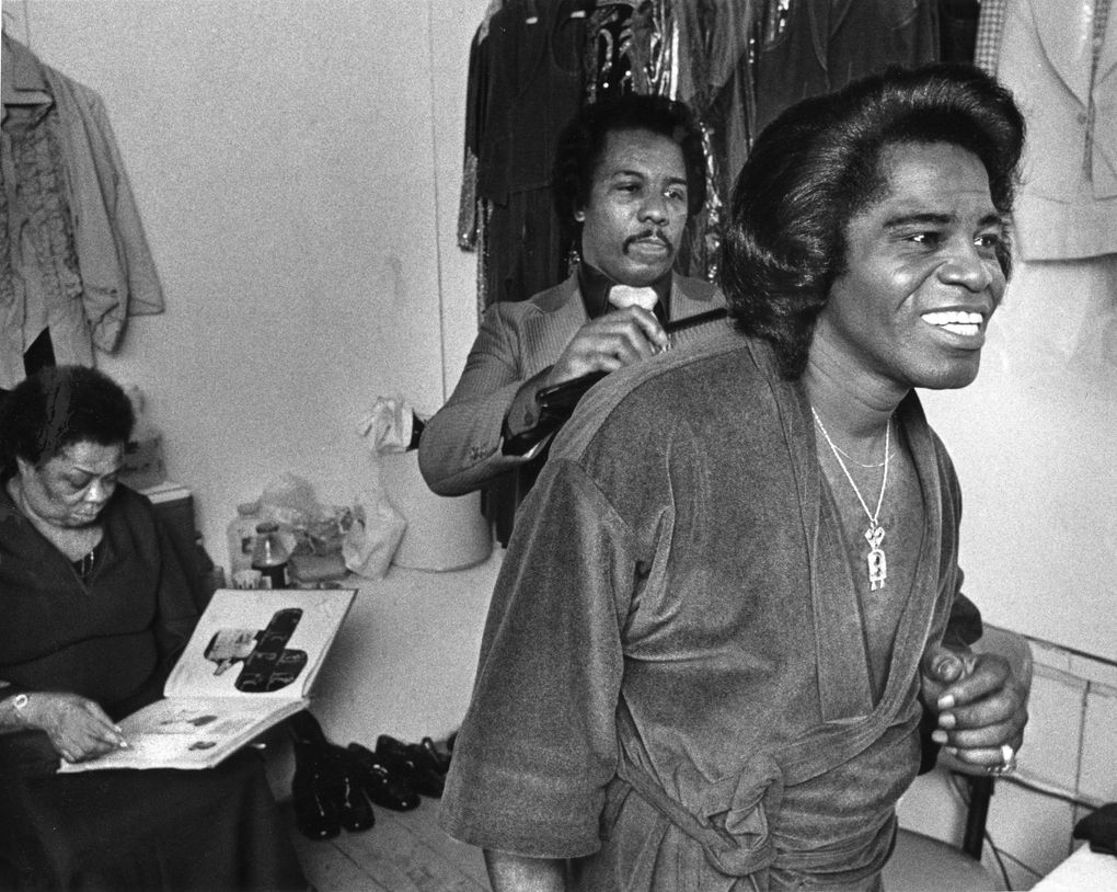 James Brown has his hair attended to by Henry Stall, his hairstylist and personal manager, as his wardrobe coordinator Gertrude Sanders waits in the background. He was primping by a mirror in his dressing room between shows at the Showbox in 1980. (Matt McVay / The Seattle Times)