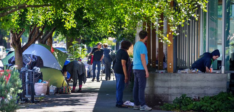 Pedestrians pause on Tuesday to observe people camping around the the Ballard Branch of the Seattle Public Library, a popular spot for the neighborhood’s homeless population. The number of homelessness people counted in Ballard quadrupled from 2017 to 2018. (Mike Siegel / The Seattle Times)