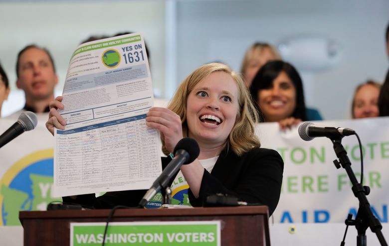 Abigail Doerr, campaign director for Yes on 1631, holds up an initiative petition with signatures on it, at a May 10, 2018, rally in Seattle. (Ted S. Warren / The Associated Press)