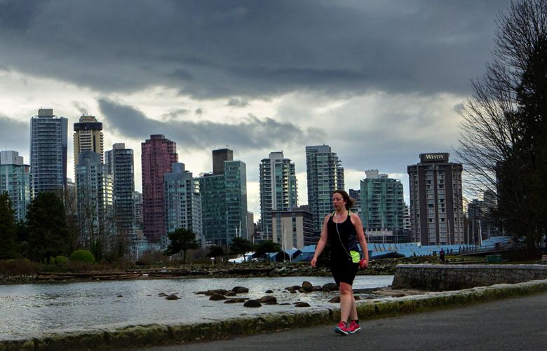 A runner cruises down the waterfront trail at Stanley Park in Vancouver, B. C. Tuesday, March 14, 2017.  The Vancouver skyline is at top of frame.
