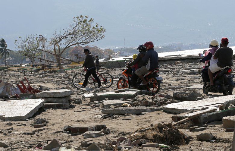 People move through rubble and debris following a massive earthquake and tsunami at Talise beach in Palu, Central Sulawesi, Indonesia, Monday, Oct. 1, 2018. A mass burial of earthquake and tsunami victims was being prepared in a hard-hit city Monday as the need for heavy equipment to dig for survivors of the disaster that struck a central Indonesian island three days ago grows desperate. (AP Photo/Tatan Syuflana) XTS129 XTS129