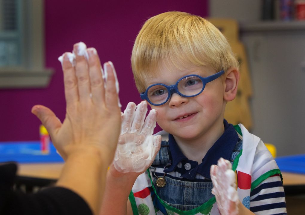 Peter Bennett high-fives occupational therapist Sommer Orgill as the two play with toy cars and shaving cream at Kindering. (Ellen M. Banner / The Seattle Times)