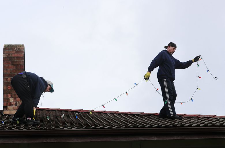 Employee Madison Murray, left, and Rob Johnston, owner of Clear N’ Bright Windows, work to install holiday lights at a home in Sultan, Wash. Thursday, Nov. 29, 2018. The business uses commercial-grade, LED lights without a fuse that can operate for years in a wet climate without needing to be replaced.   (Erika Schultz / The Seattle Times)