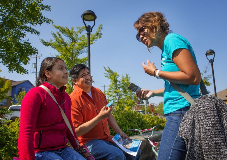 Darany Pen, right, a talent development specialist with Highline Public Schools, speaks with Roberto Santos and his daughter Alejandra Santos, 11, at a family resource fair in White Center. (Ellen M. Banner / The Seattle Times)
