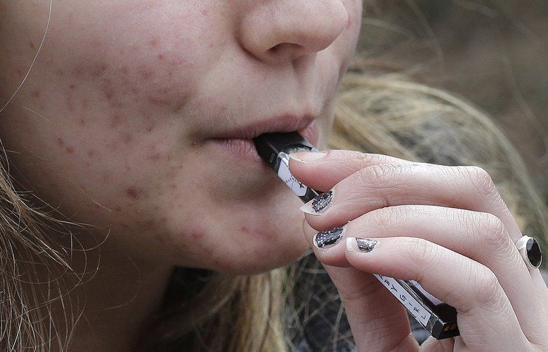 FILE – In this April 11, 2018 file photo, a high school student uses a vaping device near a school campus in Cambridge, Mass. Twice as many high school students used nicotine-tinged electronic cigarettes in 2018 compared with the previous year, an unprecedented jump in a large annual survey of teen smoking, drinking and drug use. Findings were released on Monday, Dec. 17, 2018. (AP Photo/Steven Senne, File) NY876 NY876